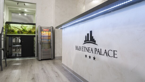 A reception area with a Coca-Cola vending machine, a fish tank, and a sign for B&B ETNEA PALACE. - B&B Etnea Palace (Catania)