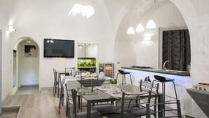 A modern dining area with a long table, chairs, a flat-screen TV, a fish tank, and a bar area with a sink and stools. - B&B Etnea Palace (Catania)