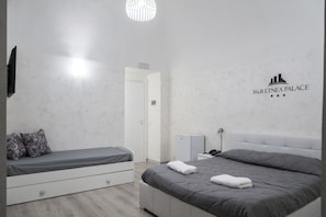 A hotel room with two beds, a white wardrobe, a desk, and a wall-mounted TV. - B&B Etnea Palace (Catania)