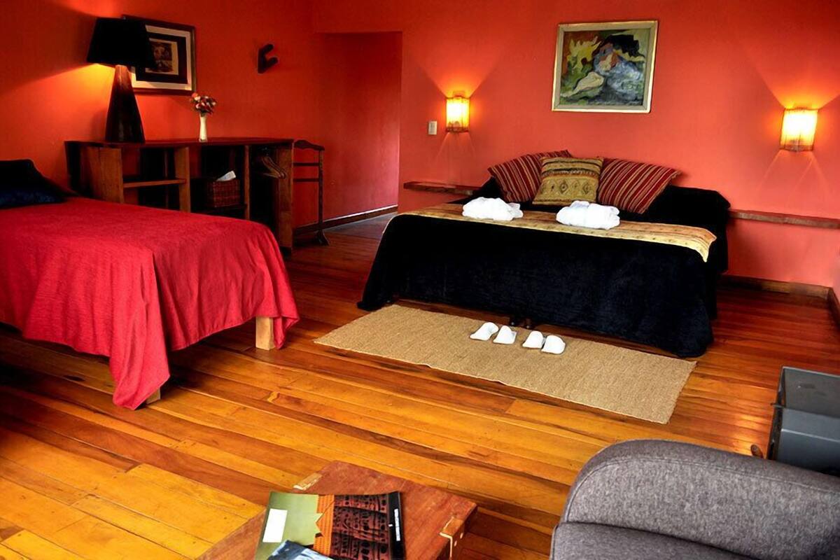 A room with a bed, a desk, and a chair. There are two wall-mounted lamps and a painting on the wall.