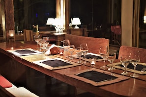A dining table set with multiple wine glasses, plates, and cutlery, with a wooden table and cushioned chairs. - El Soberbio Lodge (El Soberbio)