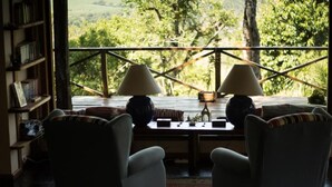 A cozy room with two armchairs, a wooden table, and a view of lush greenery through a balcony railing. - El Soberbio Lodge (El Soberbio)