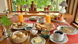 A breakfast table with various food items, drinks, and a Buddha statue in the background. - El Soberbio Lodge (El Soberbio)