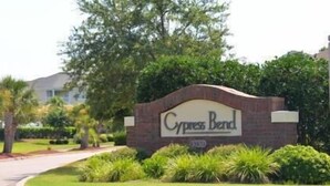 En skylt för Cypress Bend, med en mur av tegelstenar och grönska runt omkring.