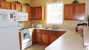 A kitchen with wooden cabinets, a white refrigerator, a microwave, a stove, a sink, and a window with blinds. - 911 Willow Bend (North Myrtle Beach)