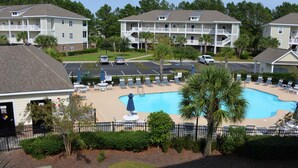 A pool area with lounge chairs and umbrellas, surrounded by a fence and palm trees. - 911 Willow Bend (North Myrtle Beach)