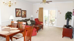 A dining area with a wooden table and chairs, a red armchair, a sofa, and a ceiling fan. - 911 Willow Bend (North Myrtle Beach)