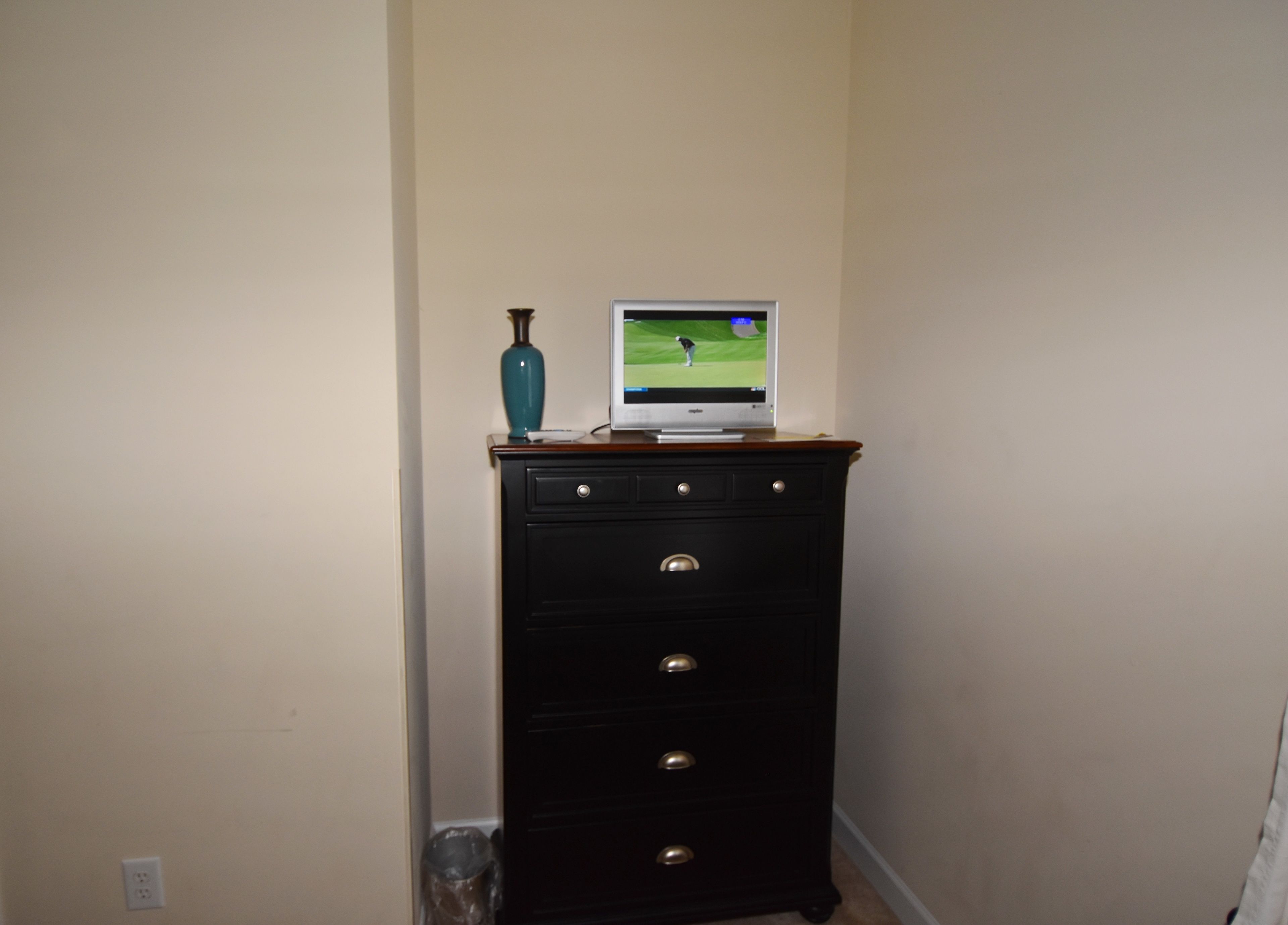 Een zwarte dressoir met lades en een televisie erboven waarop een golfwedstrijd wordt vertoond.
