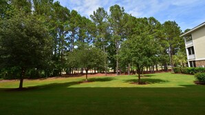 A well-maintained lawn with a row of tall trees and a building with a balcony in the background. - 612 Willow Bend (North Myrtle Beach)