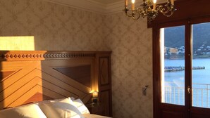 A hotel room with a large bed, a wooden headboard, a chandelier, and a view of a body of water through a door. - Hotel Boutique Mar d'Amunt (Port de la Selva)