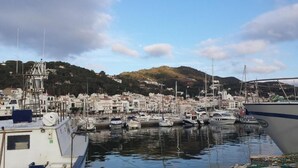 A marina with boats docked, a town in the background, and a hill with buildings. - Hotel Boutique Mar d'Amunt (Port de la Selva)