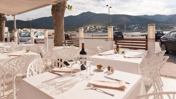 An outdoor dining area with white tables and chairs, set against a backdrop of mountains and a body of water. - Hotel Boutique Mar d'Amunt (Port de la Selva)
