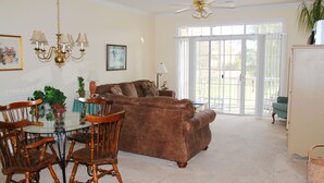A living room with a brown sofa, wooden chairs, a glass dining table, and a ceiling fan. - 223 Wedgewood (North Myrtle Beach)