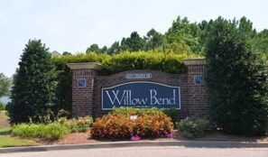 A sign for Willow Bend with a brick wall and greenery.