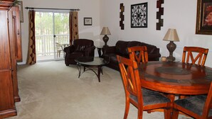 A living room with a wooden dining table, two leather sofas, a glass coffee table, and a large window with curtains. - 432 Willow Bend (North Myrtle Beach)