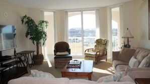 A spacious living room with a large window, a television, a sofa, a coffee table, and a potted plant.