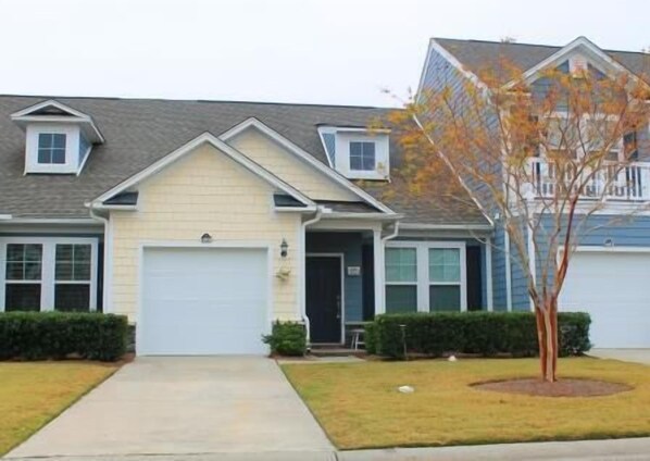 A two-story residential building with a garage, a small front yard, and a tree.