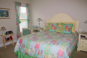 A bedroom with a bed, a nightstand, a lamp, a dresser, and a window with curtains.