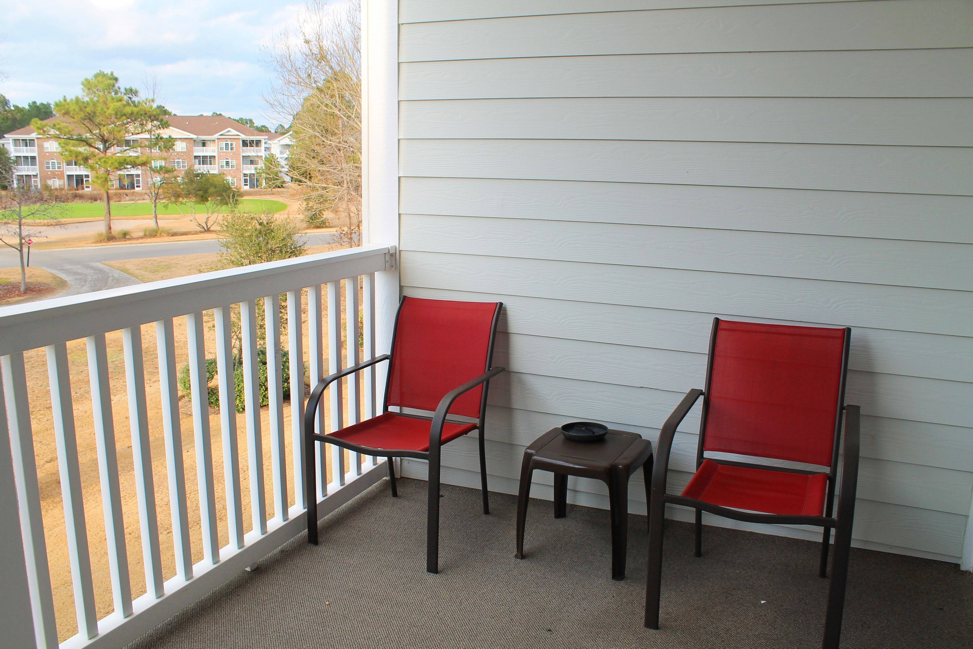 Un balcon avec deux chaises rouges et une petite table, donnant sur un quartier résidentiel.