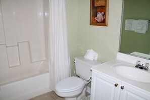 A bathroom with a white toilet, a bathtub, a sink with a mirror, and a shower curtain. - 522 Ironwood (North Myrtle Beach)