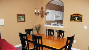 A dining area with a wooden table and black chairs, a chandelier, a framed picture, and a sign for 'The 19th Hole Bar & Grill'. - 522 Ironwood (North Myrtle Beach)