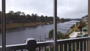 A river view from a balcony with a railing, a small boat on the water, and buildings along the riverbank. - 332 Edgewater (North Myrtle Beach)