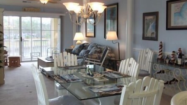 A spacious living room with a glass coffee table, white chairs, a sofa, and a chandelier. - 332 Edgewater (North Myrtle Beach)