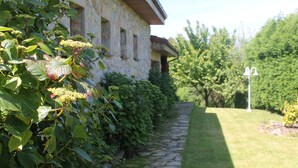 A stone pathway leading to a stone building with a garden and a bell post.