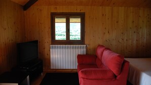 A room with wooden walls, a red sofa, a TV on a stand, and a window with a view of greenery.