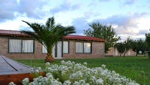 A brick building with a red roof, white curtains, and a palm tree in the foreground. - Finca Fisterra (Fray Luis Beltrán)