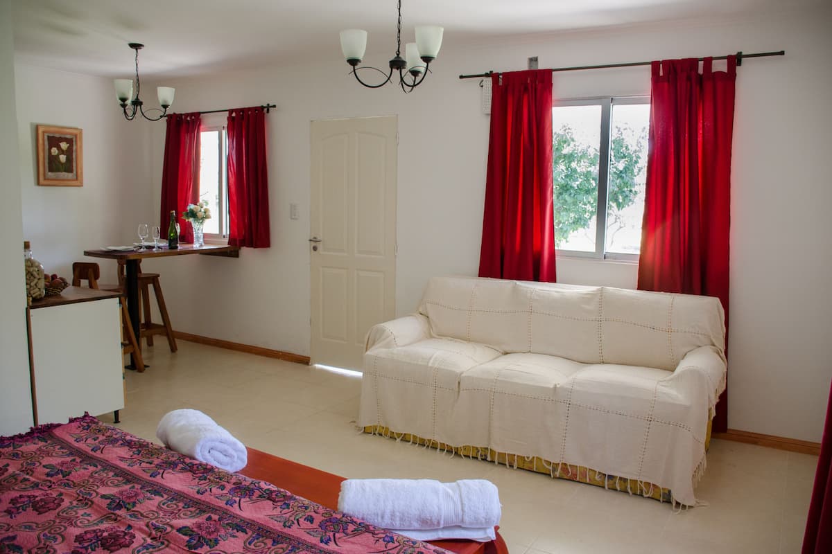 Une pièce comprenant un lit, un canapé, un bureau avec une chaise, une fenêtre avec des rideaux rouges et un lustre.