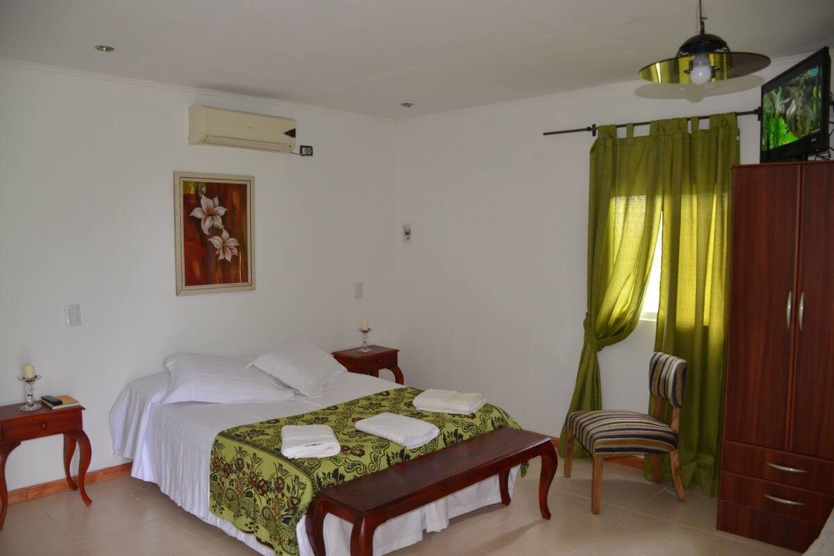 Une chambre à coucher comprenant un lit, un banc, une chaise, une armoire, une table de chevet et un tableau accroché au mur.