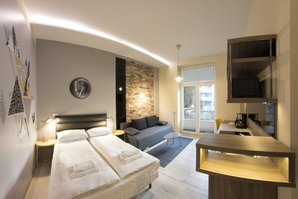 A modern hotel room with a large bed, a sofa, a dining table, and a TV.