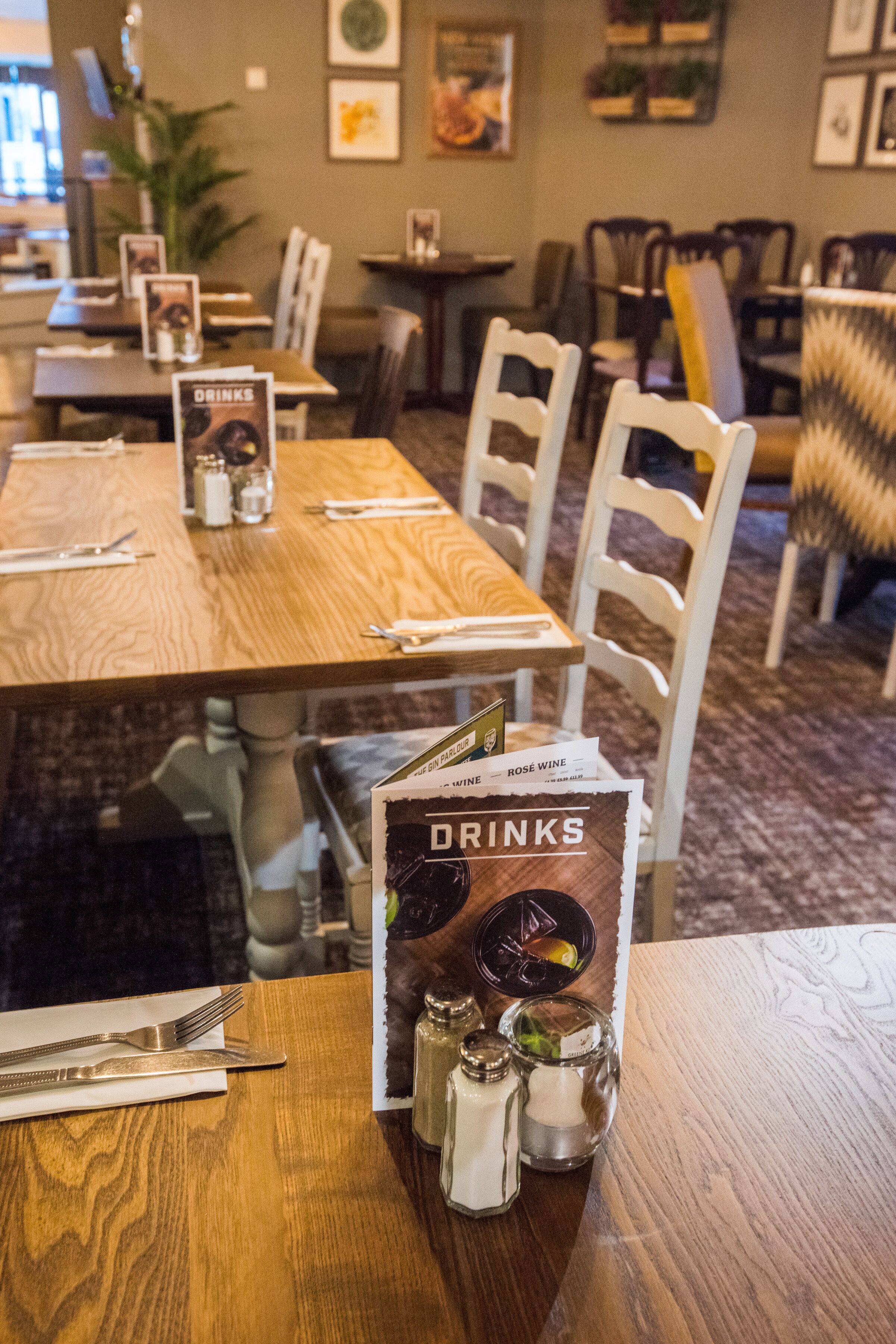 A dining area with wooden tables, white chairs, and a menu stand displaying a drinks menu.