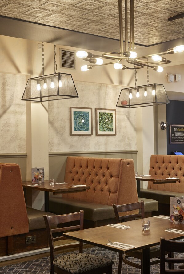 Interior de restaurante con cabinas, mesas y lámparas colgantes.