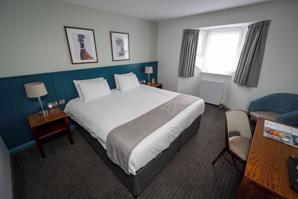 A hotel room with a large bed, two bedside tables with lamps, a chair, and a window with curtains.