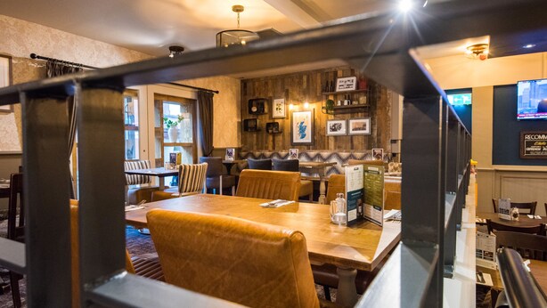 Un restaurante con mesas y sillas de madera, una zona de bar y una pantalla de televisión en la pared.