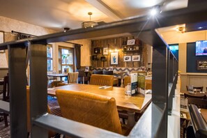 Un restaurante con mesas y sillas de madera, una zona de bar y una pantalla de televisión en la pared.