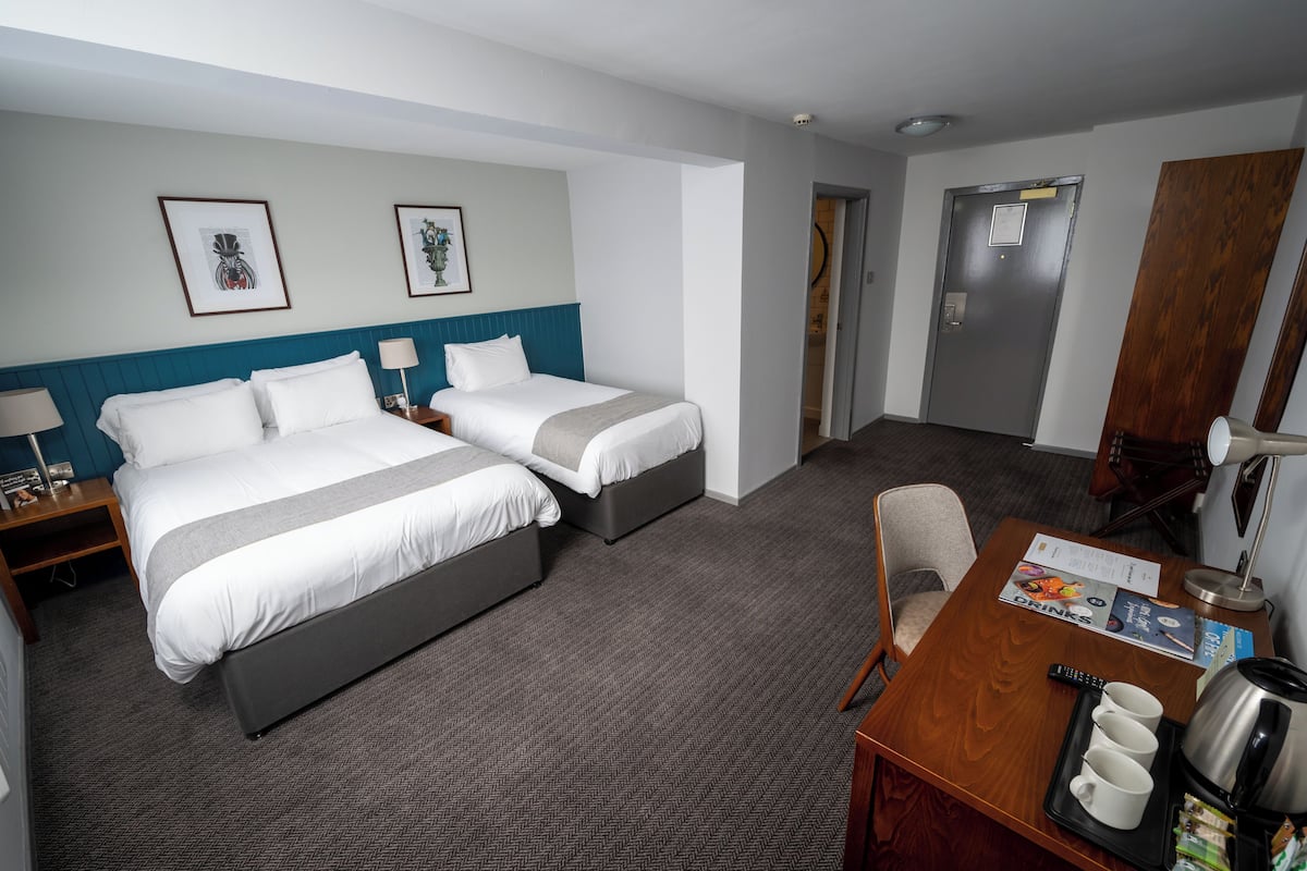A hotel room with two beds, a desk with a coffee maker, and framed artwork on the wall.
