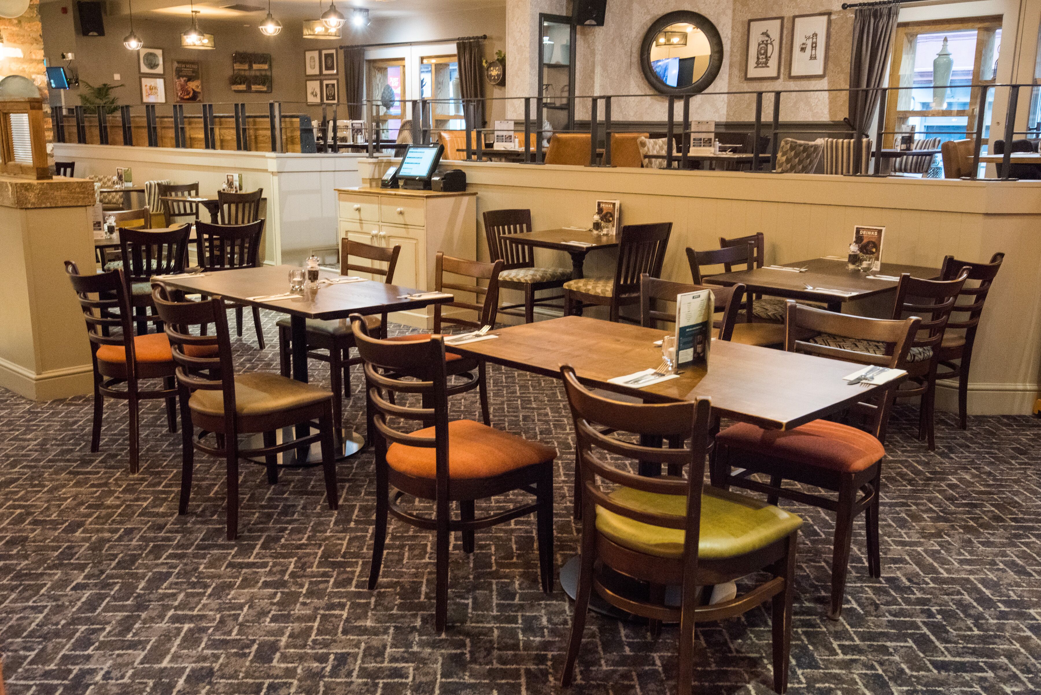 A restaurant with multiple wooden tables and chairs, a counter with a menu, and a brick-patterned floor.