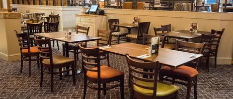 A restaurant with multiple wooden tables and chairs, a counter with a menu, and a brick-patterned floor.