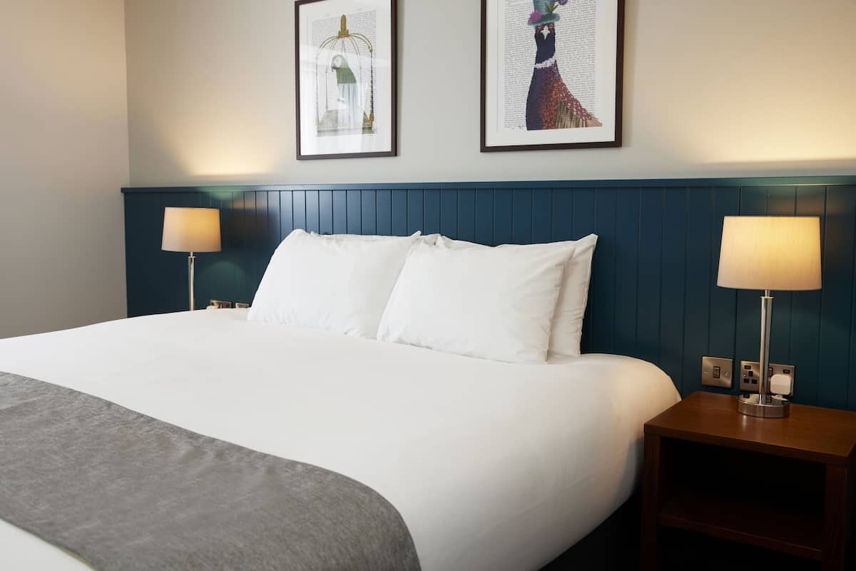 A neatly made bed with white linens, two bedside lamps, and two framed artworks on the wall.