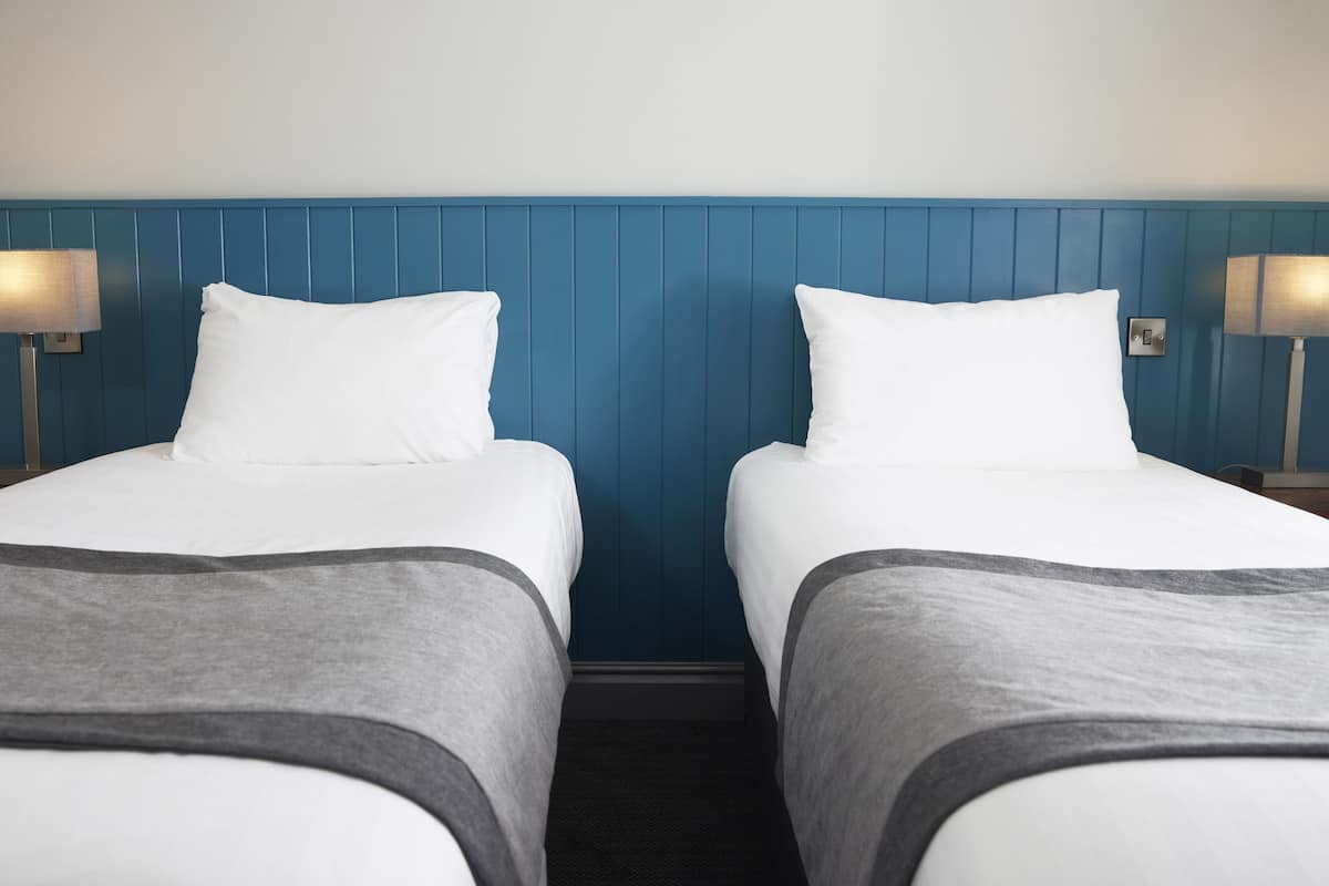 A hotel room with two beds, a blue headboard, and bedside lamps.