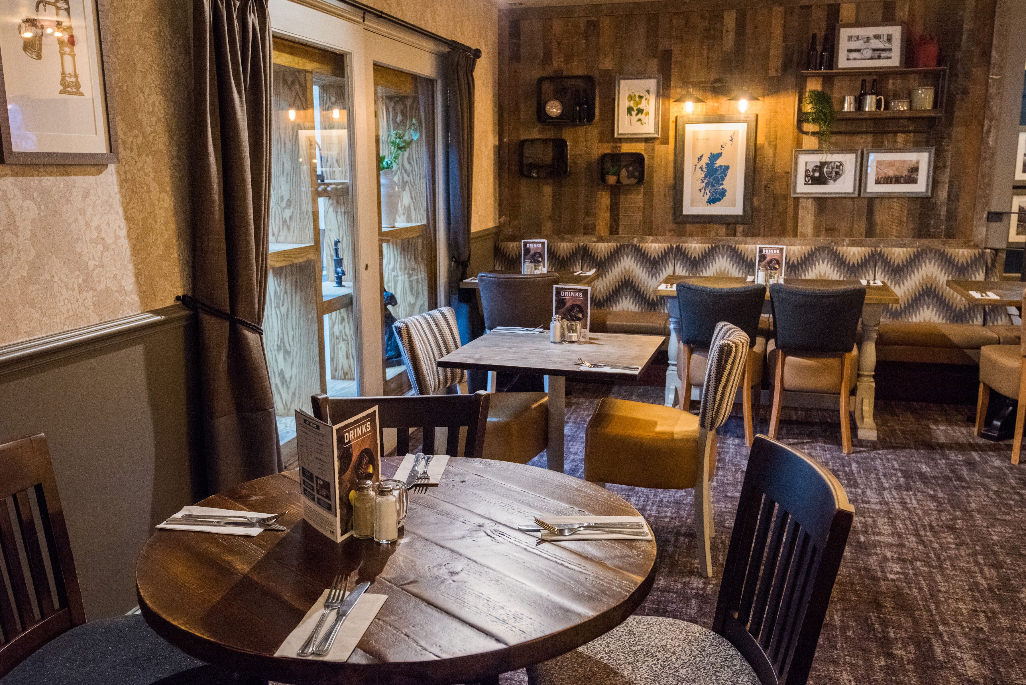 Un restaurante con mesas y sillas de madera, un atril para el menú y cuadros en la pared.