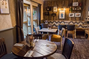 Un restaurante con mesas y sillas de madera, un atril para el menú y cuadros en la pared.