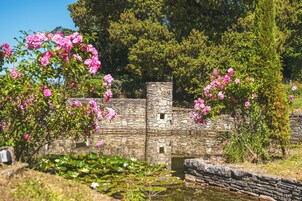 A stone structure with a small window, surrounded by lush greenery and pink flowers.