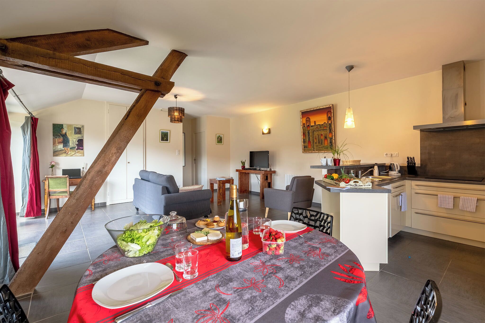 A dining area with a table set for a meal, a kitchen in the background, and a staircase leading to another room.