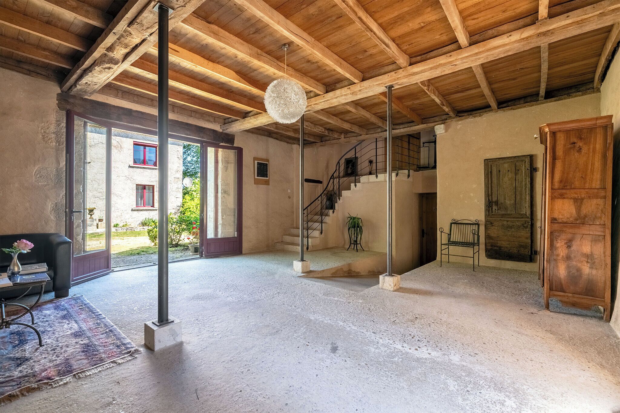 A spacious room with a high ceiling, a staircase, and a view of the outside.