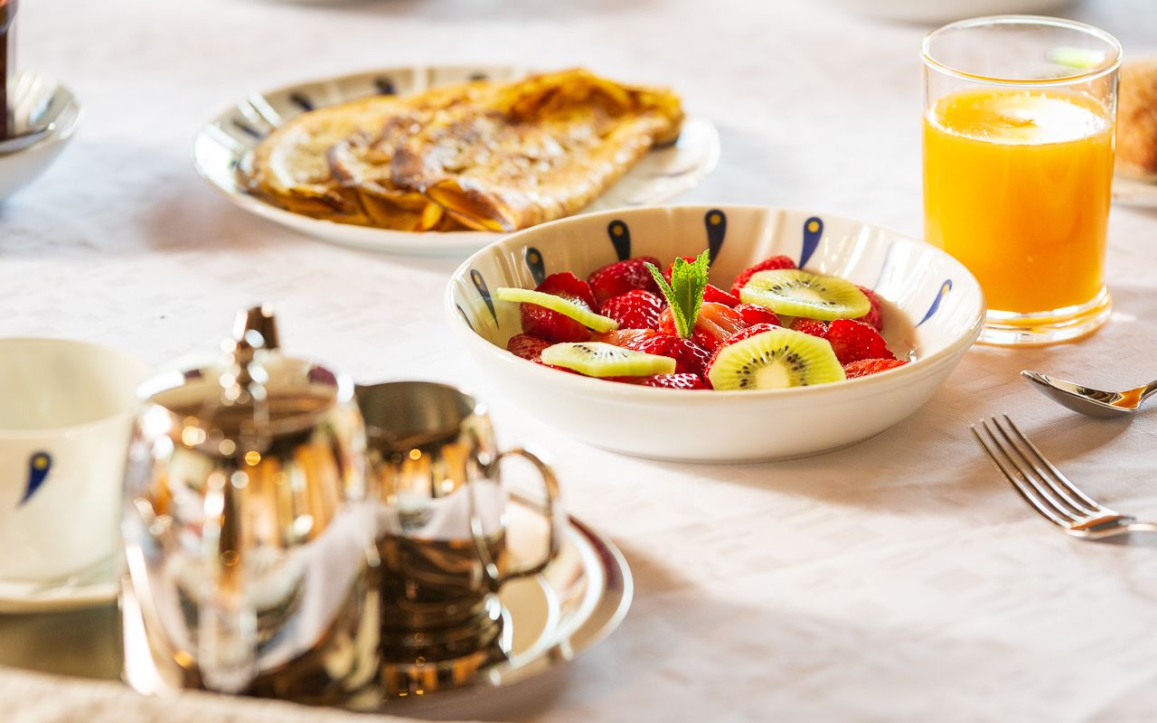 A breakfast setting with a bowl of fruit salad, a glass of orange juice, and a plate of crepes.