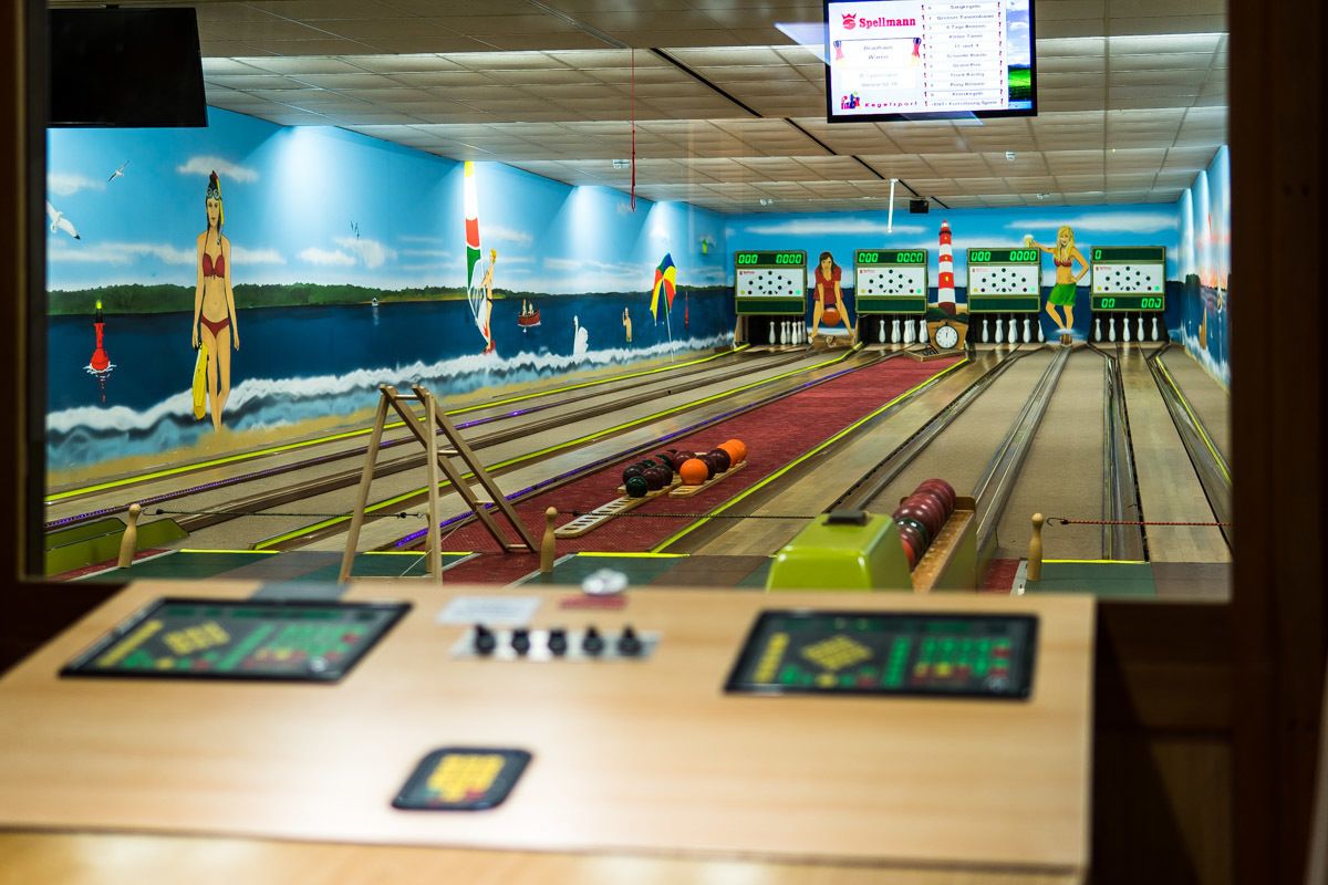 Een bowlingbaan met een muurschildering van een strand en een scorebord.